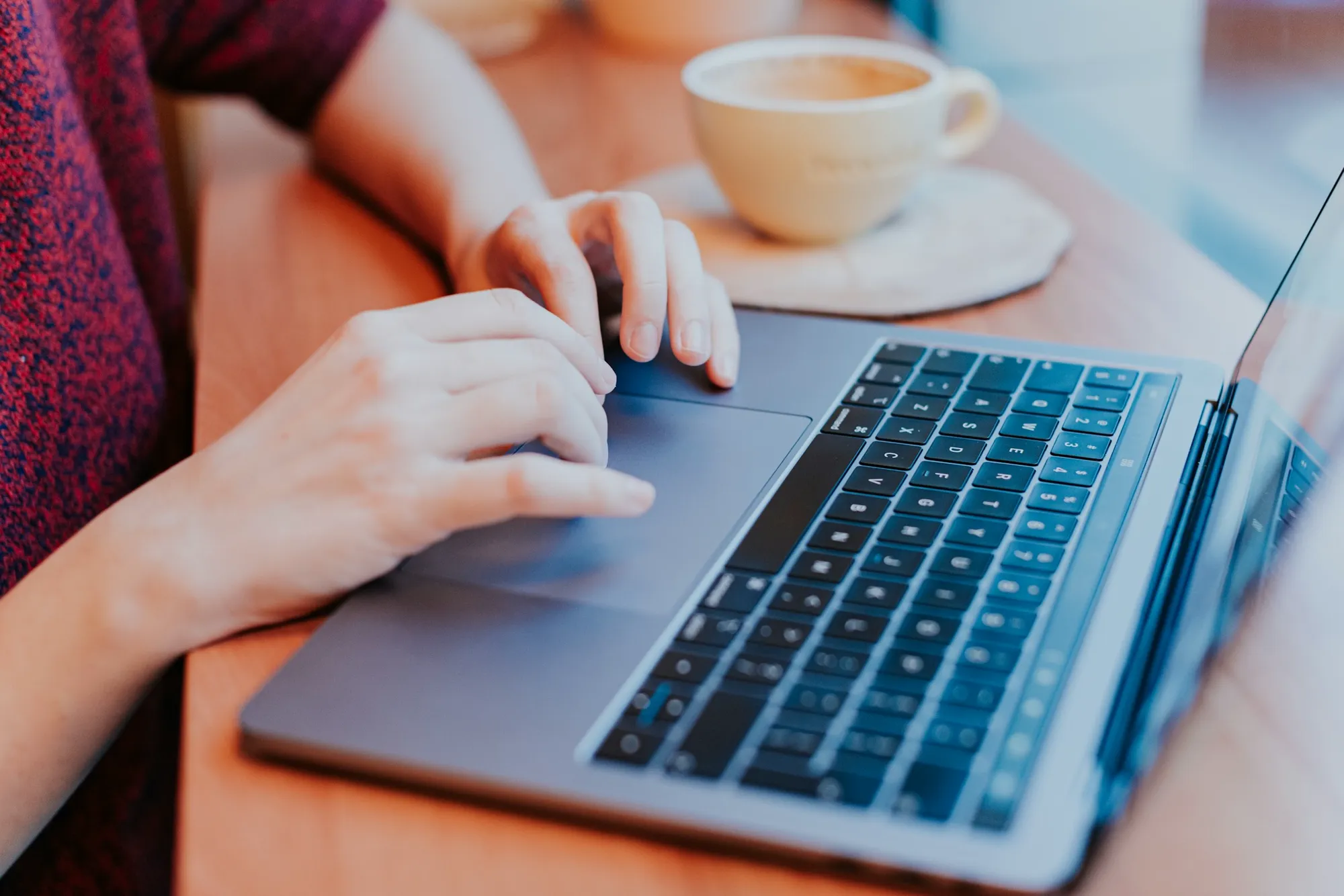 A hand scrolling on a laptop trackpad beside a cup of coffee